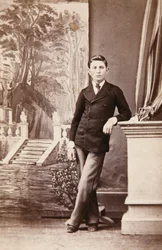 Studio-Porträt eines jungen Mannes vor gemaltem Hintergrund mit Treppe und Garten